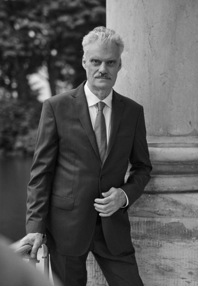 Profesor Zbigniew Wawer stoi przy kolumnie, ubrany w garnitur. 