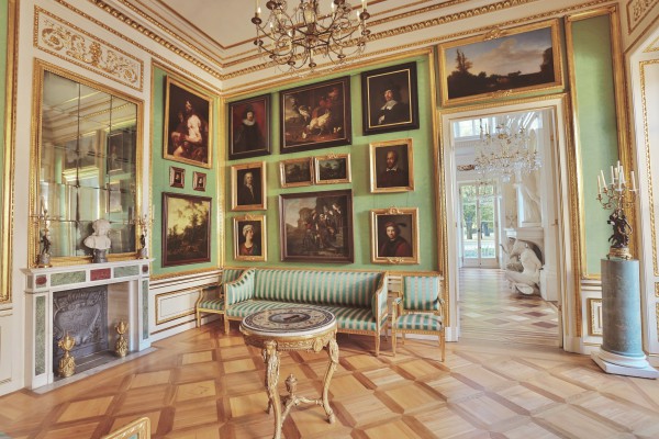Gabinet portretowy w Pałacu na Wyspie. Ściany zdobią obrazy, na jednej z nich, po lewej, znajduje się kominek, nad którym wisi lustro. W pomieszczeniu stoi kanapa i stolik.
