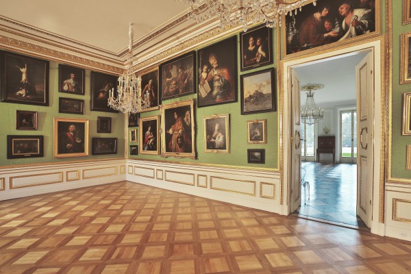 Galeria Obrazów w Pałacu na Wyspie. Na ścianach wiszą portrety i obrazy przedstawiające krajobraz. Na ścianie, po prawej, znajdują się drzwi. 