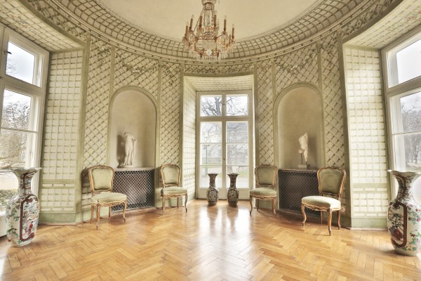 Buduar w Pałacu Myślewickim, na półokrągłych ścianach znadują się okna, po ścianami stoją krzesła i wazy, w dwóch niszach ściennych ekspnowane są rzeźby. 