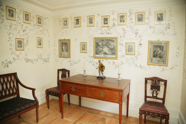 Pokoik, w którym stoją stół krzesła, a na ścianach wiszą obrazy.