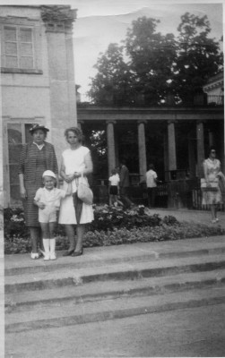 Archiwalne zdjęcie przedstawiające dwie kobiety i dziecko, którzy stoją na schodach przed Pałacem na Wyspie.