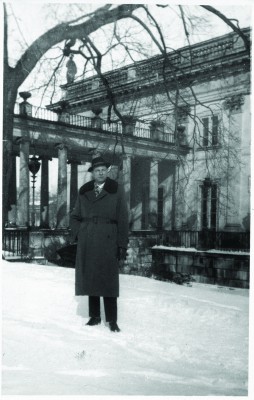 Mężczyzna w płaszczu i kapeluszu stoi przed Pałacem na Wyspie zimą.