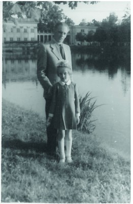 Dziecko z mężczyzną stoi nad stawem w Łazienkach, w tle widać Pałac na Wyspie.