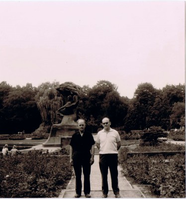 Dwóch mężczyzn pozuje na tle Pomnika Chopina w Łazienkach Królewskich.