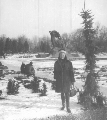 Kobieta stoi i pozuje do zdjęcia zimą w Łazienkach, w tle widać Pomnik Fryderyka Chopina.