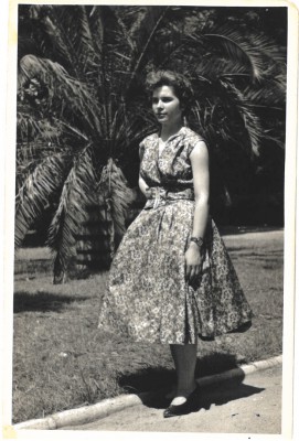 Kobieta stoi w ogrodzie, w tle widać palmę. 