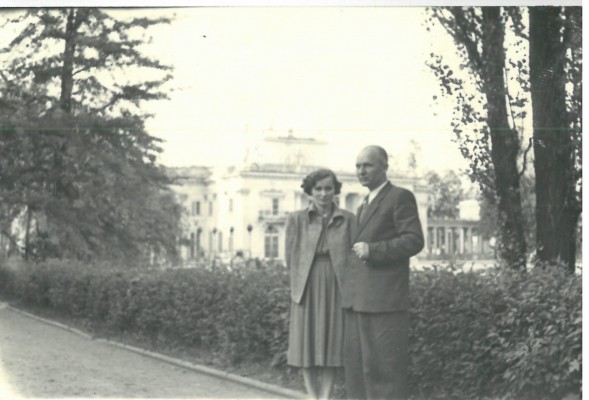 Kobieta i mężczyzna stoją na ścieżce w Łazienkach, w tle widać Pałac na Wyspie w otoczeniu drzew.