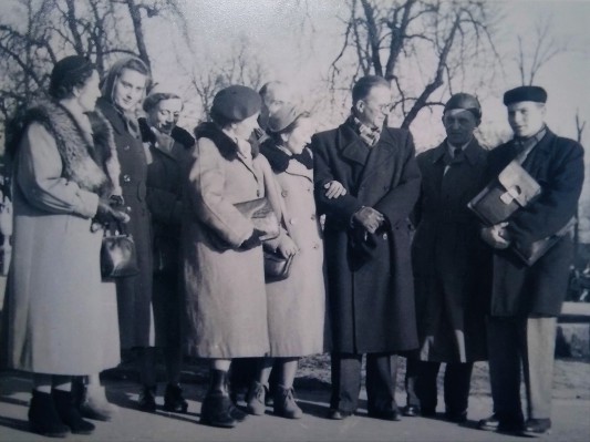  Archiwalne zdjęcie przedstawiające grupę kobiet i mężczyzn w zimowych płaszczach, którzy stoją na parkowej alejce w Łazienkach Królewskich. 