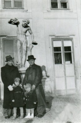 Dwóch mężczyzn i dwóch kilkuletnich chłopców stoi pod rzeźbą na tle fasady Pałacu na Wyspie.