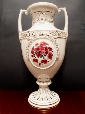 Porcelanowy biały wazon z namalowanymi pośrodku czerwonymi kwiatami. 