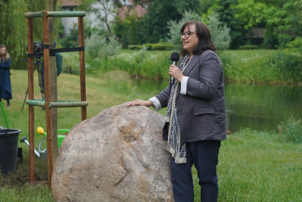 Kobieta stoi przy kamieniu z mikrofonem w ręku. 