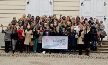 Kilkadziesiąt kobiet stoi przed budynkiem, pozując do pamiątkowego zdjęcia.