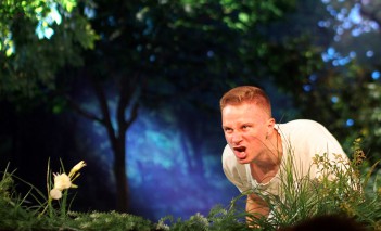 Scena w teatrze stylizowana na las, mężczyzna klęczy i wydaje z siebie okrzyk.