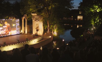 Widok na Amfiteatr w Łazienkach Królewkich, w otoczeniu drzew, nocą, podświetlony światłem lamp.