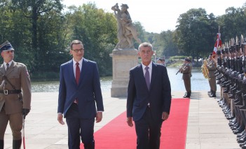 Premier Morawiecki i premier Babisz idą po czerwonym dywanie, po lewej i prawej stronie stoją żołnierze pełniący wartę honorową.