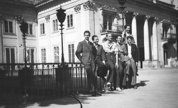 Archiwalne zdjęcie przedstawiające grupę mężczyzn opierających się o barierkę na tarasie Pałacu na Wyspie.