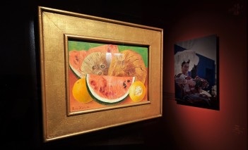 Obraz wiszący na ścianie, który przedstawia martwą naturę. Na obrazie widoczne są dwie pomarańcze, między nimi kawałek arbuza, powyżej kokosy. 