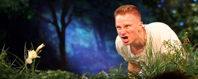 Scena w teatrze stylizowana na las, mężczyzna klęczy i wydaje z siebie okrzyk.