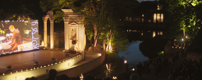 Widok na Amfiteatr w Łazienkach Królewkich, w otoczeniu drzew, nocą, podświetlony światłem lamp.