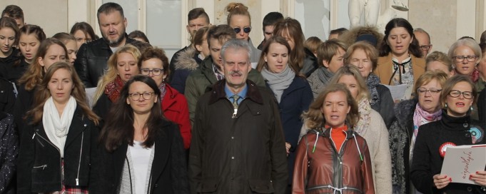 Grupa osób stoi obok siebie na baczność i śpiewa.