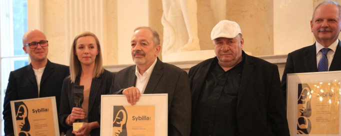 Trzech mężczyzn pozuje do zdjęcia, mężczyźni z lewej i prawej strony trzymają w rękach dyplomy.