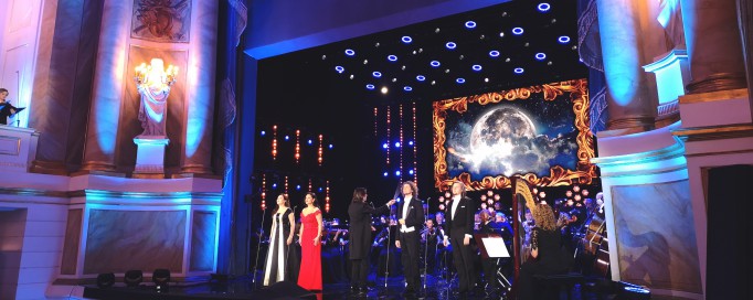 Koncert w Teatrze Królewskim. Na scenie znajduje się orkiestra i soliści, widać fragment widowni. 