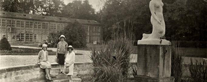 Rok 1927. Trzy kobiety przy sadzawce na tle budynku Starej Oranżerii w Łazienkach Królewskich. Obok przy sadzawce znajduje się rzeźba na postumencie przedstawiająca klęczącą, nagą kobietę.