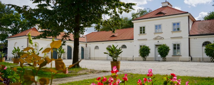 Budynek Stajni Kubickiego. Przed budynkiem na trawniku rosną czerwone kwiaty. 