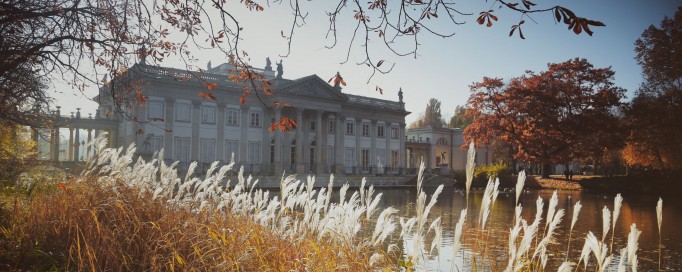 Widok na Pałac na Wyspie w otoczeniu wody i jesiennej roślinności.
