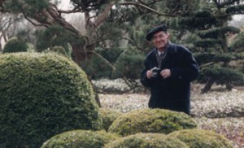 Starszy mężczyzna stoi w ogrodzie wśród krzewów.