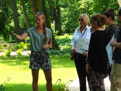 Grupa dorosłych osób stojąca w ogrodach Łazienek Królewskich. 