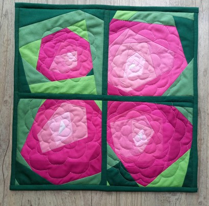 Kawałek kwadratowej tkaniny ozdobionej czterema różowymi różami wykonanymi z materiału. 
