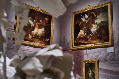 Na ścianie wiszą dwa obrazy przedstawiające ptactwo, poniżej, pod obrazem po prawej, wisi obraz przedstawiający siedzącą kobietę w sukni z epoki. 