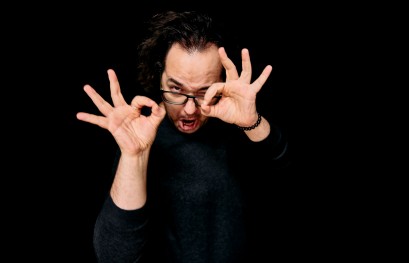 Mężczyzna ubrany na czarno trzyma uniesione ręce przy twarzy.