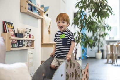 Mały chłopiec bawi się w pokoju z zabawkami na małej zjeżdżalni. 