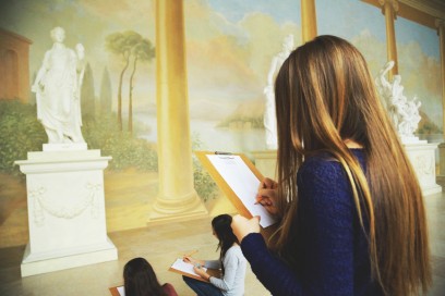 Trzy dziewczyny przed rzeźbą przedstawiającą kobietę owiniętą w szaty szkicują posąg.