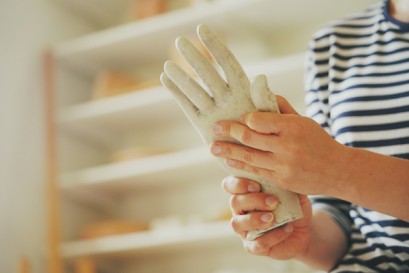 Widoczne są kobiece dłonie trzymające dłoń wykonaną z gipsu. 