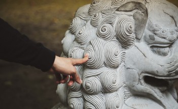 Ręka dotykająca rzeźbę przedstawiającą głowę lwa.
