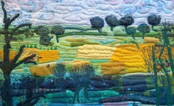 Obraz przedstawiający krajobraz, wykonany z różnych materiałów. Widoczne jest niebo, poniżej drzewa i pola. 