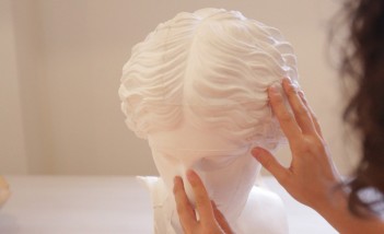 Kobiece dłonie dotykające białą wyrzeźbioną głowę kobiety. 