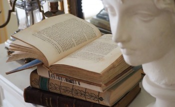 Książki leżące jedna na drugiej, obok stoi biała rzeźba przedstawiająca kobiecą głowę. 