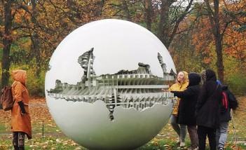 Grupa kobiet stoi przy dużej, okrągłej kuli, która stoi w parku. 