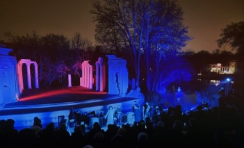 Scena na wolnym powietrzu otoczona kawałkami murów. Jest noc, scena jest podświetlona na niebiesko. Przed sceną widać tłum. 