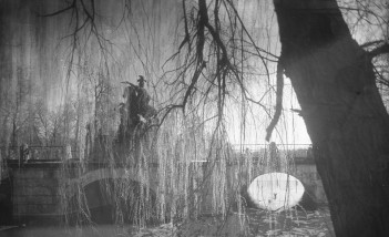 Archiwalne zdjęcie przedstawiające pomnik jeźdźca na koniu, stojący na moście na tle drzew.