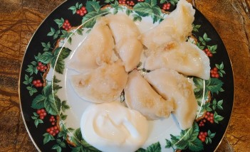 Talerz, na którym leży siedem pierogów ze skwarkami.