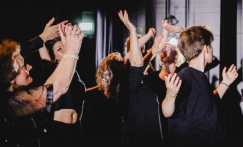 Grupa ludzi z uniesionymi w górze rękami. 