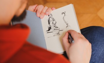 Osoba siedząca tyłem i rysująca elementy pomnika. 