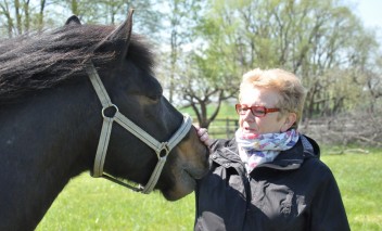Starsza kobieta stojąca przy koniu.