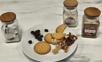 Ciasta i kawałki orzechów leżące talerzu, obok talerza stoją trzy szklane pojemniczki z przyprawami.